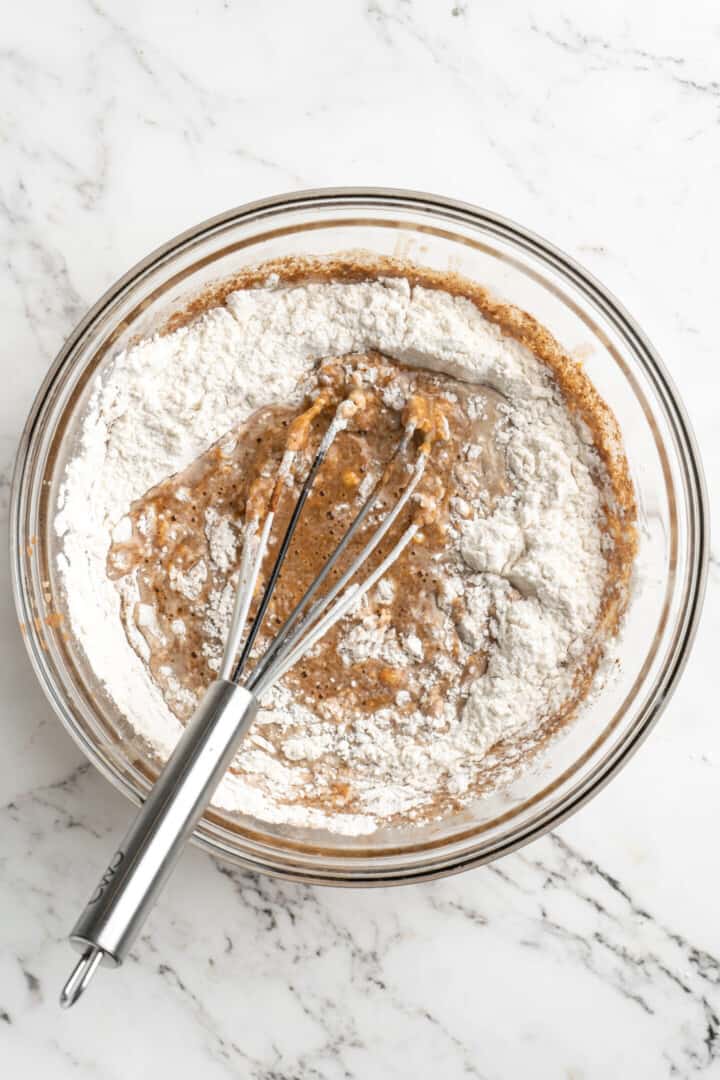 Overhead view of a mixing bowl with a whisk mixing flour into almond milk and pumpkin puree.