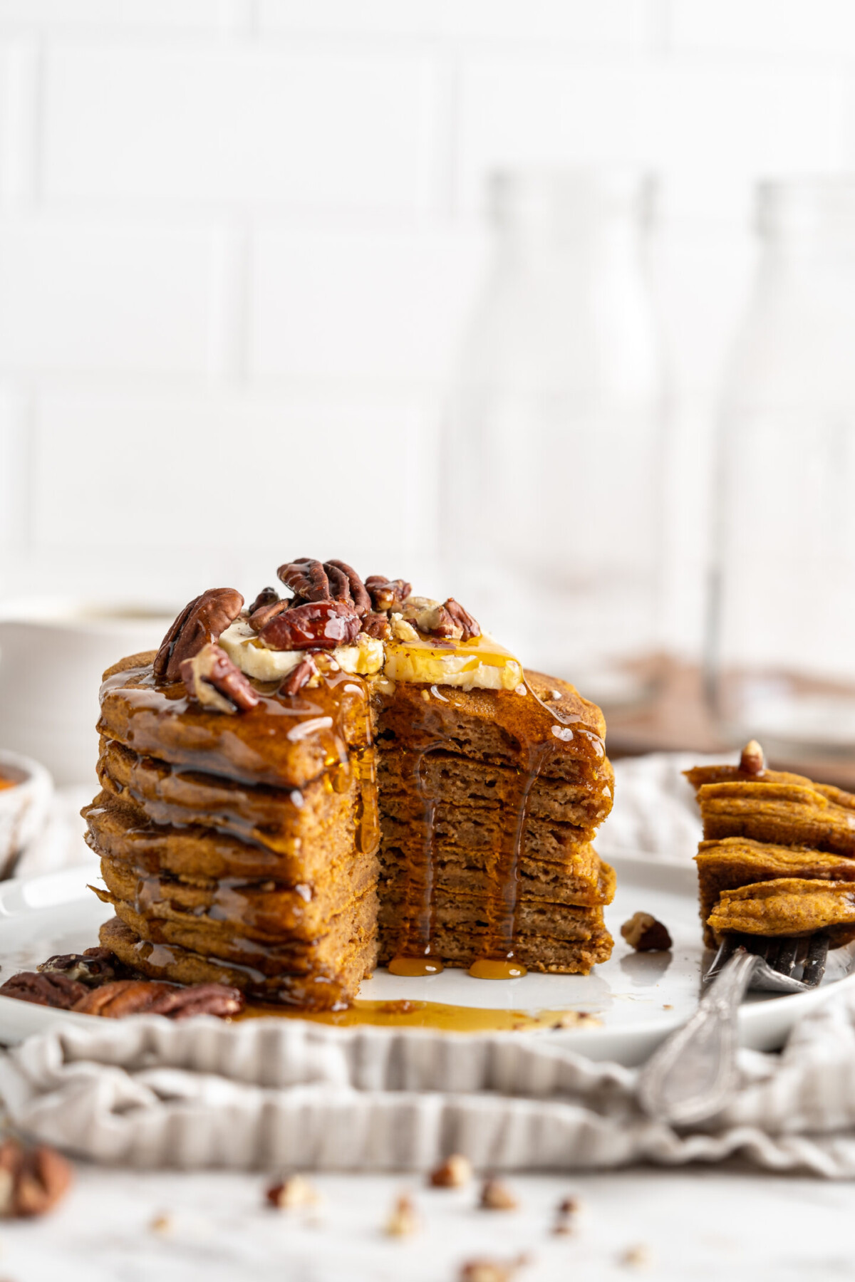 A stack of pumpkin pancakes on a plate, topped with nuts, with a quarter of the stack cut out.