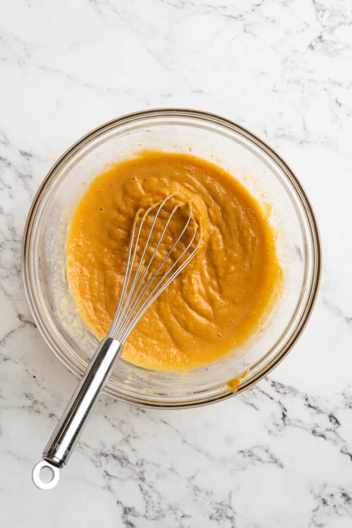Overhead view of a pumpkin puree mixture in a mixing bowl with a whisk.