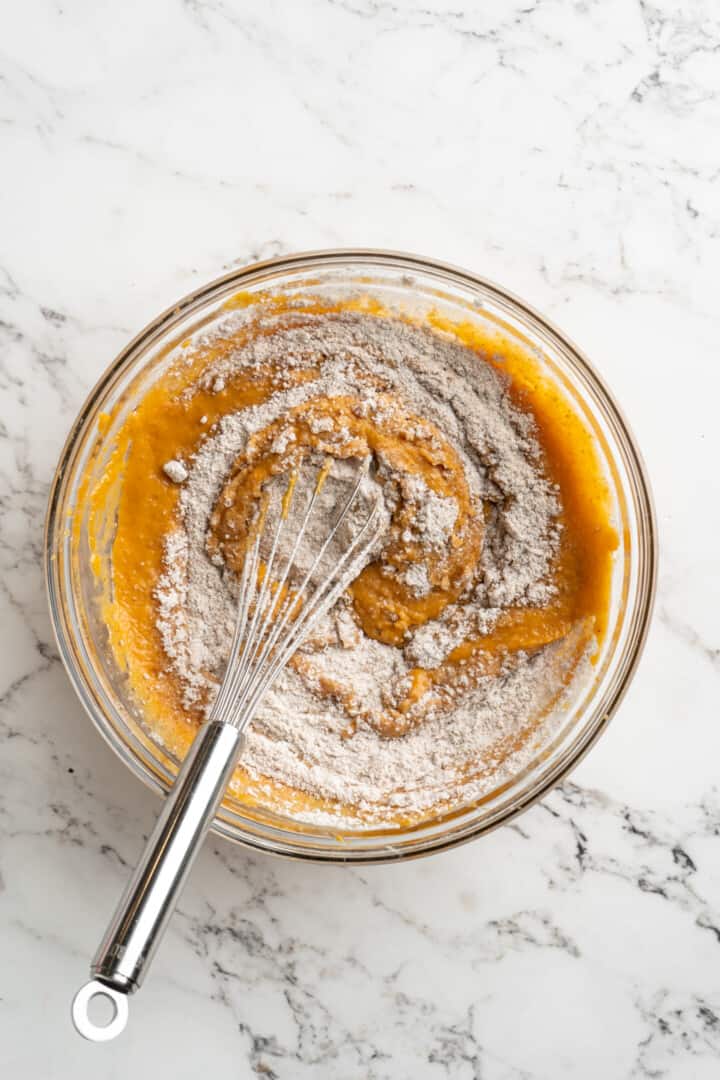 Overhead view of a whisk mixing flour into a bowl of pumpkin puree.