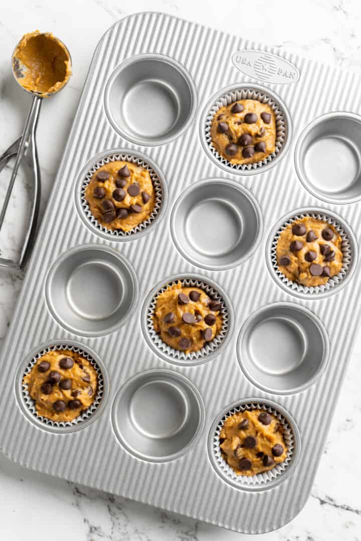 Overhead view of a muffin tray with six muffin tins filled with pumpkin chocolate chip batter.