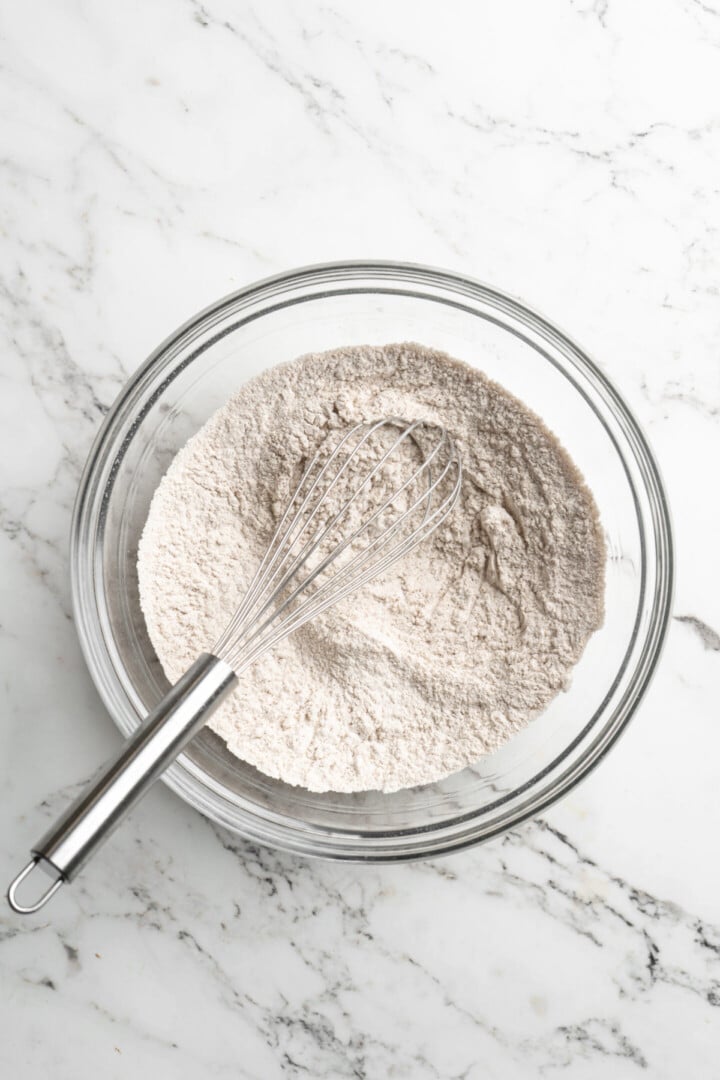 A mixing bowl with flour and other dry ingredients and a whisk