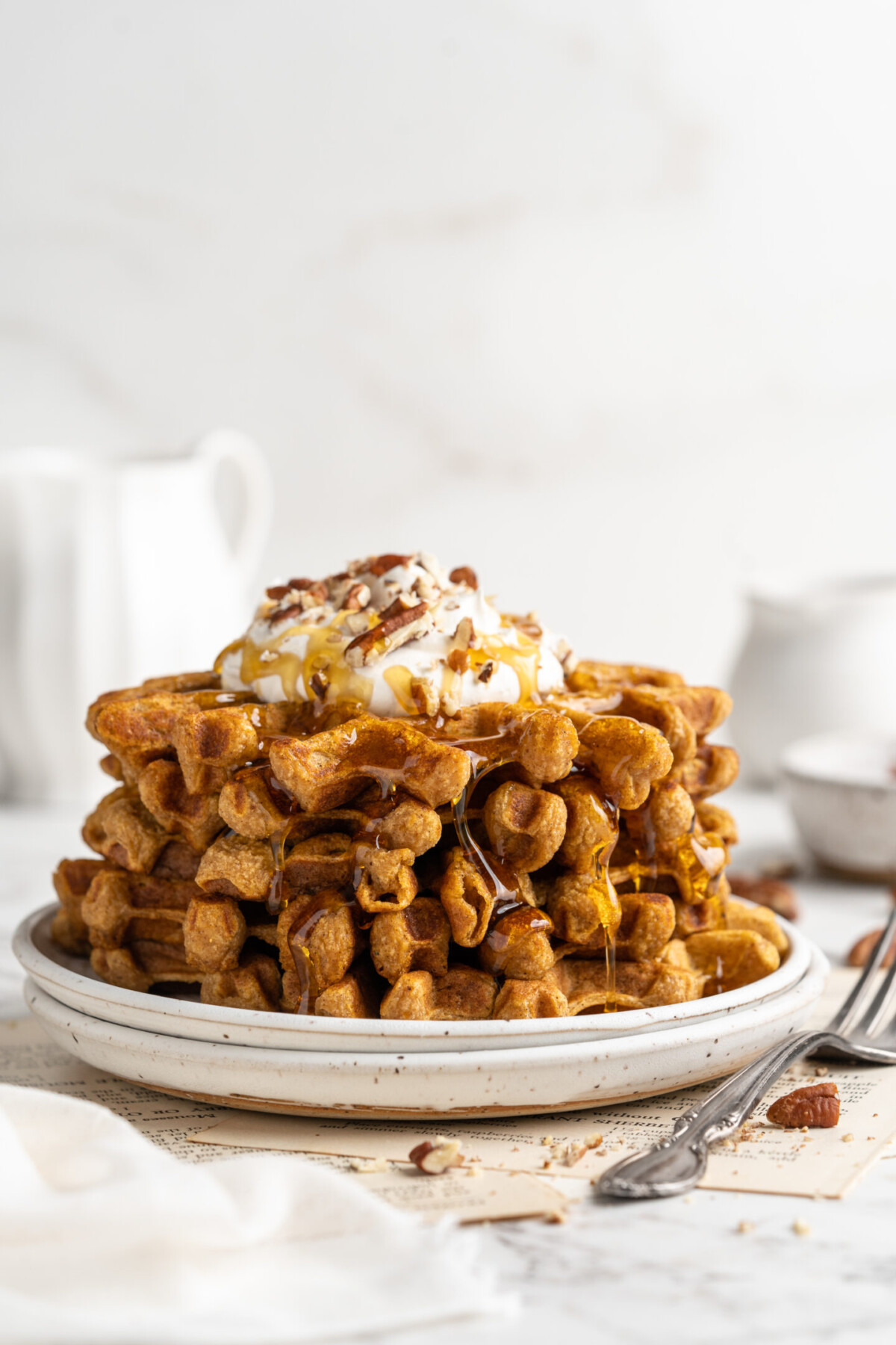 A stack of pumpkin waffles topped with coconut cream and candied pecans