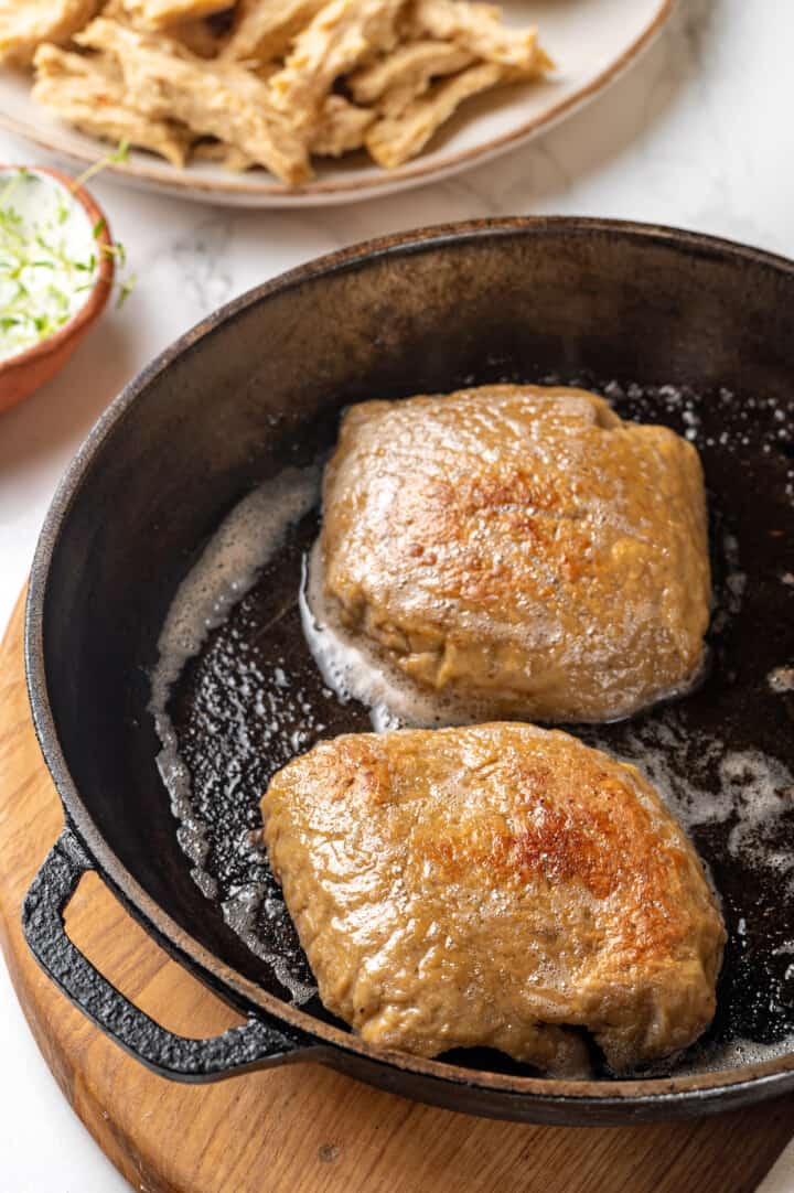 Two vegan chicken breasts being cooked in cast iron skillet