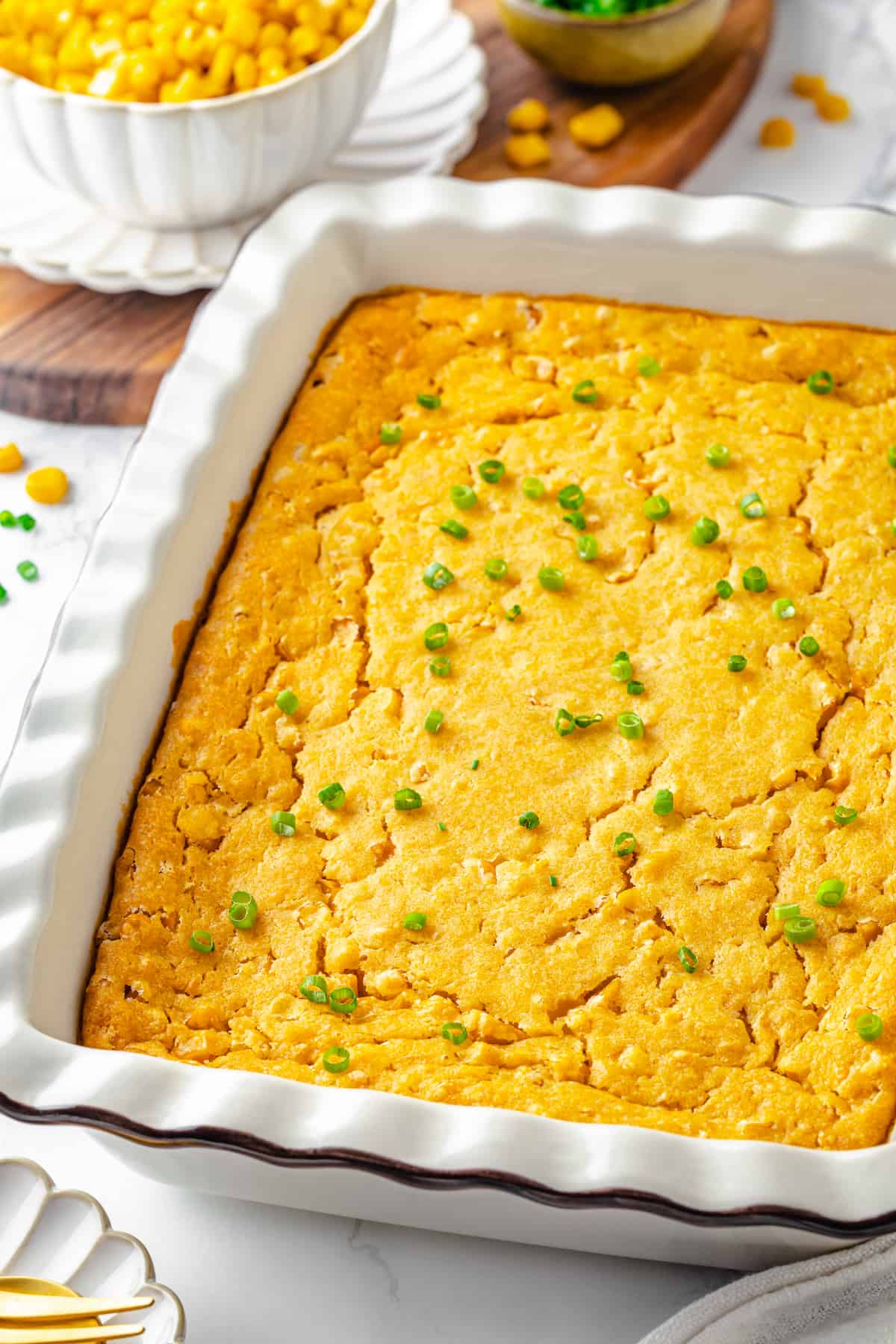 Cornbread pudding in white casserole dish with green onions scattered over top