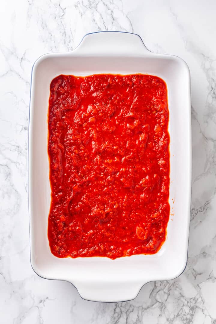 Overhead view of marinara sauce spread in the bottom of a baking dish