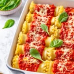 Spinach ricotta lasagna rolls in blue ceramic baking dish, with fresh basil leaves scattered on top as garnish