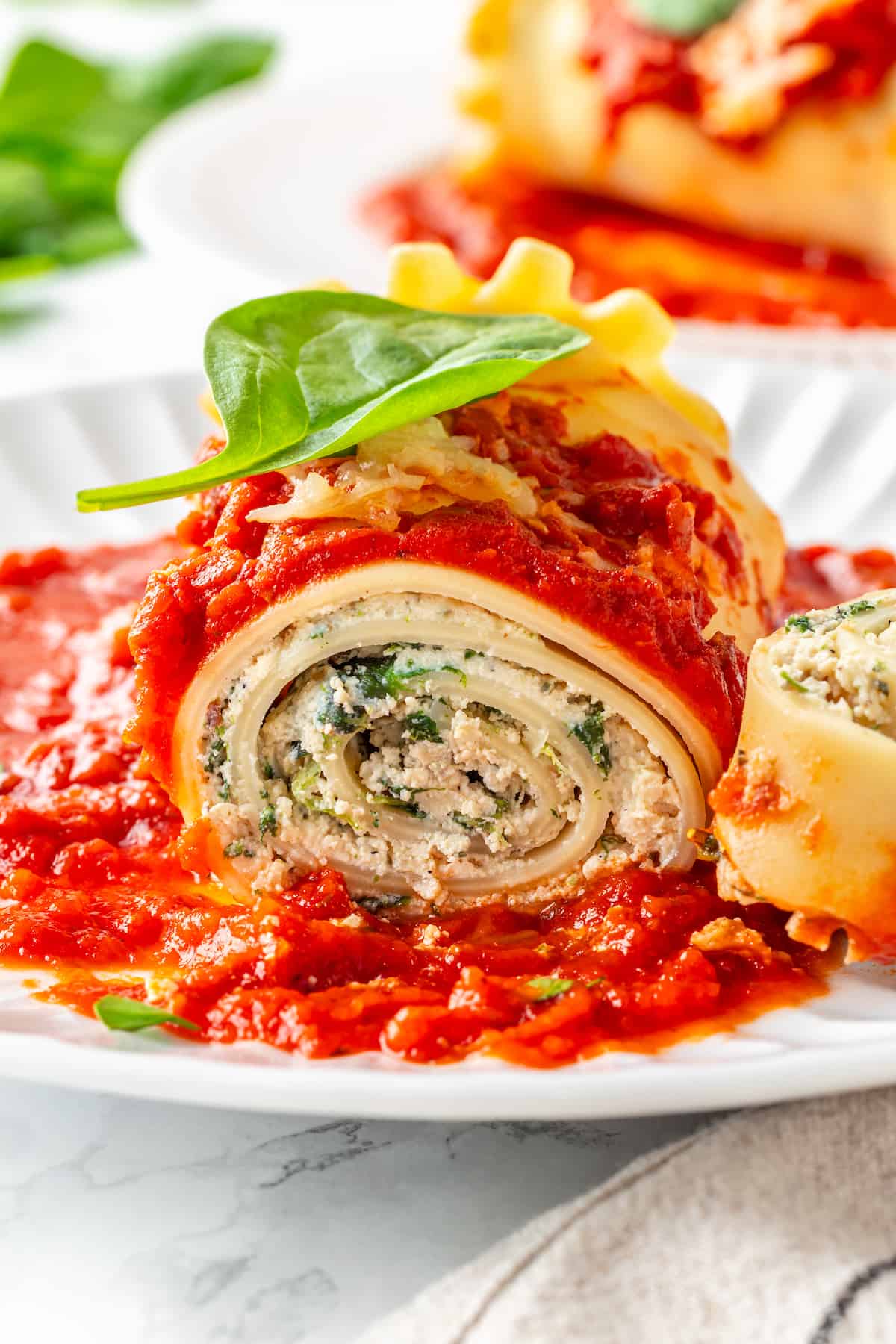 Closeup of vegan lasagna roll on plate topped with basil leaf