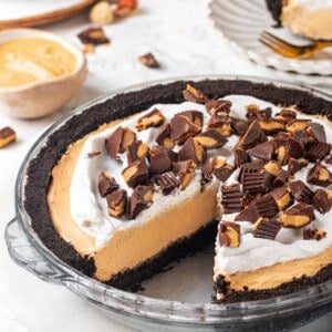 No-bake peanut butter pie topped with peanut butter cups in glass pie plate with one slice removed