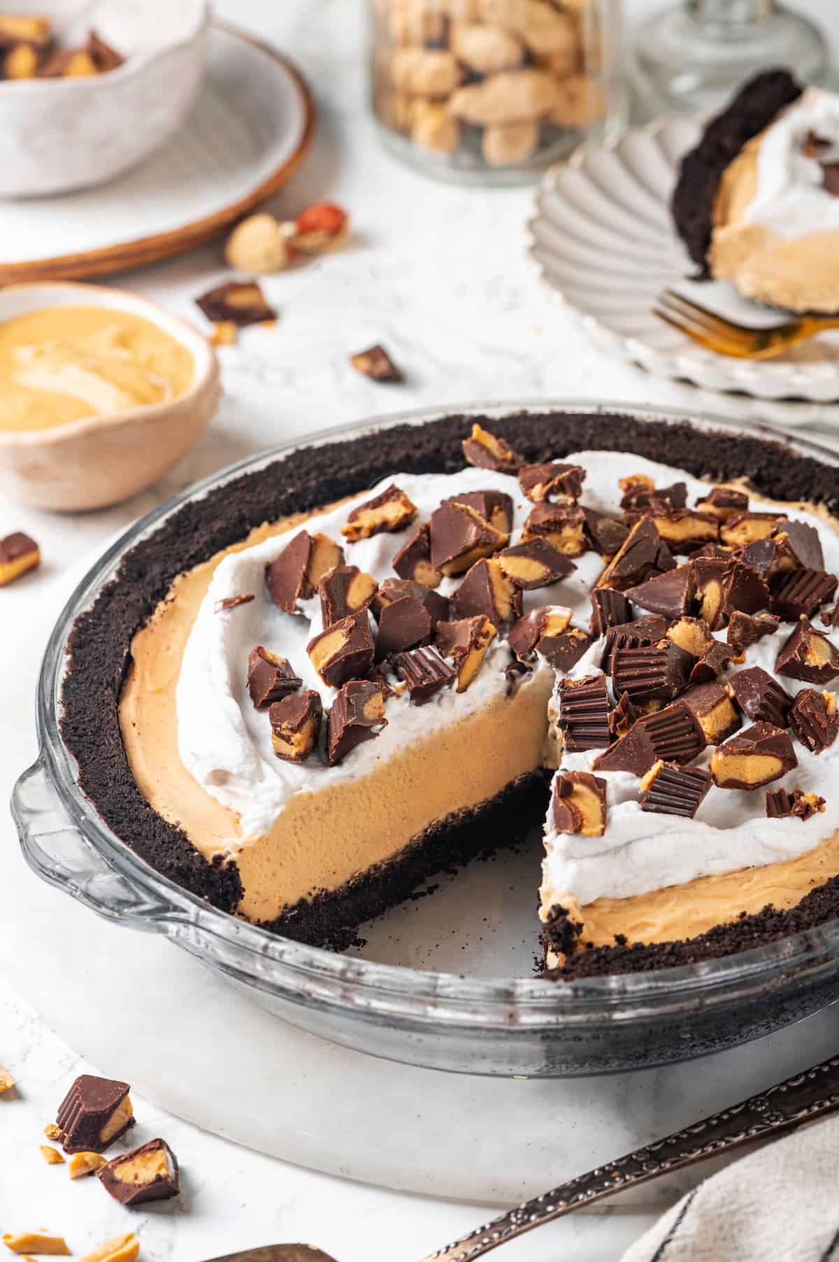 No-bake peanut butter pie topped with peanut butter cups in glass pie plate with one slice removed