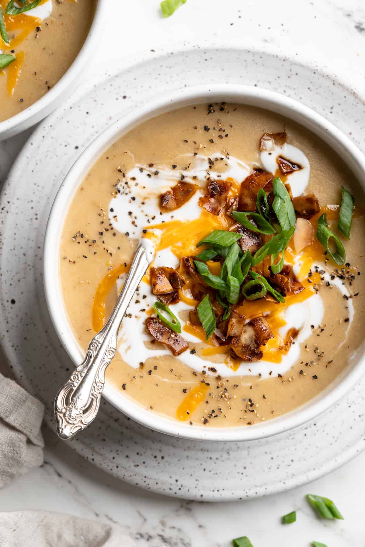 Overhead view of loaded potato soup in bowl, topped with vegan cheese, yogurt, bacon, and scallions
