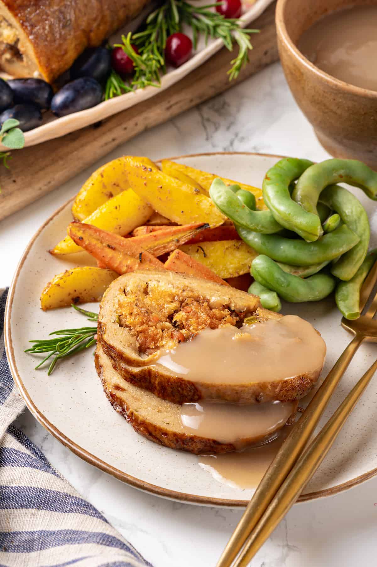 Vegan turkey slices on plate with gravy, roasted vegetables, and edamame