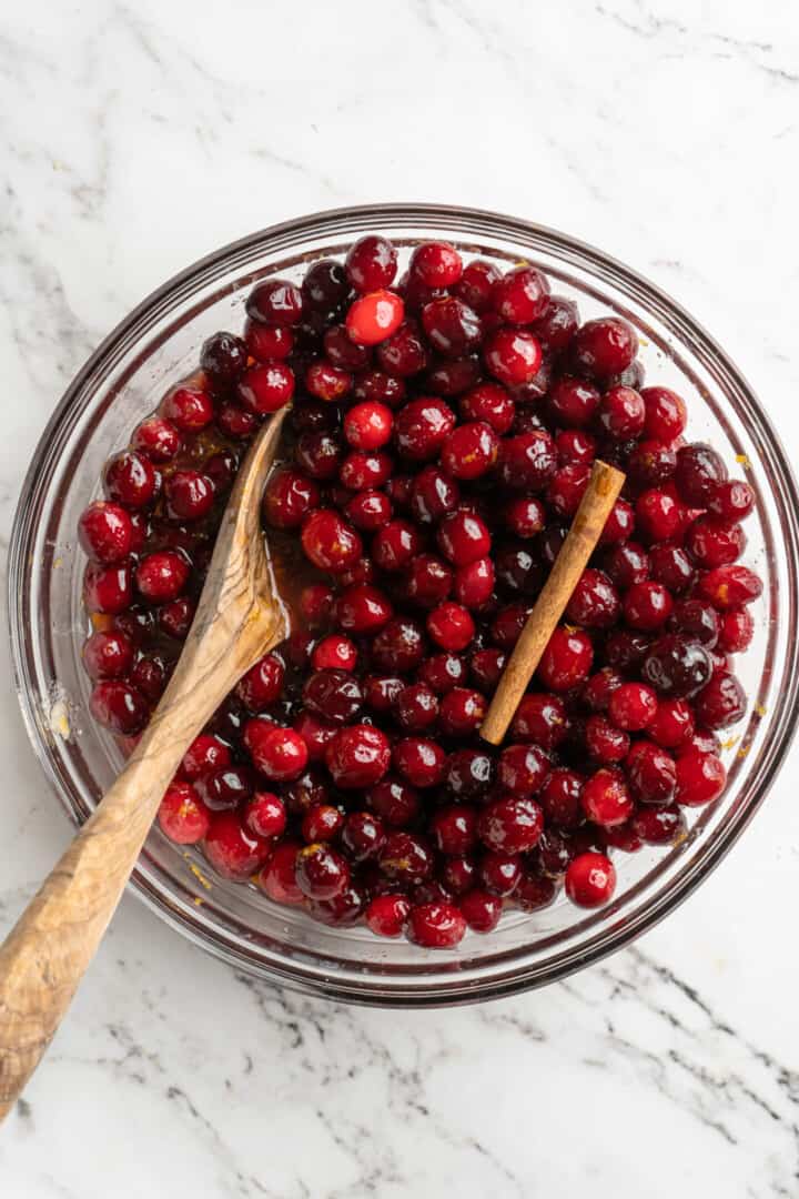 Overhead view of cranberries and cinnamon stick in glass bowl with wooden spoon
