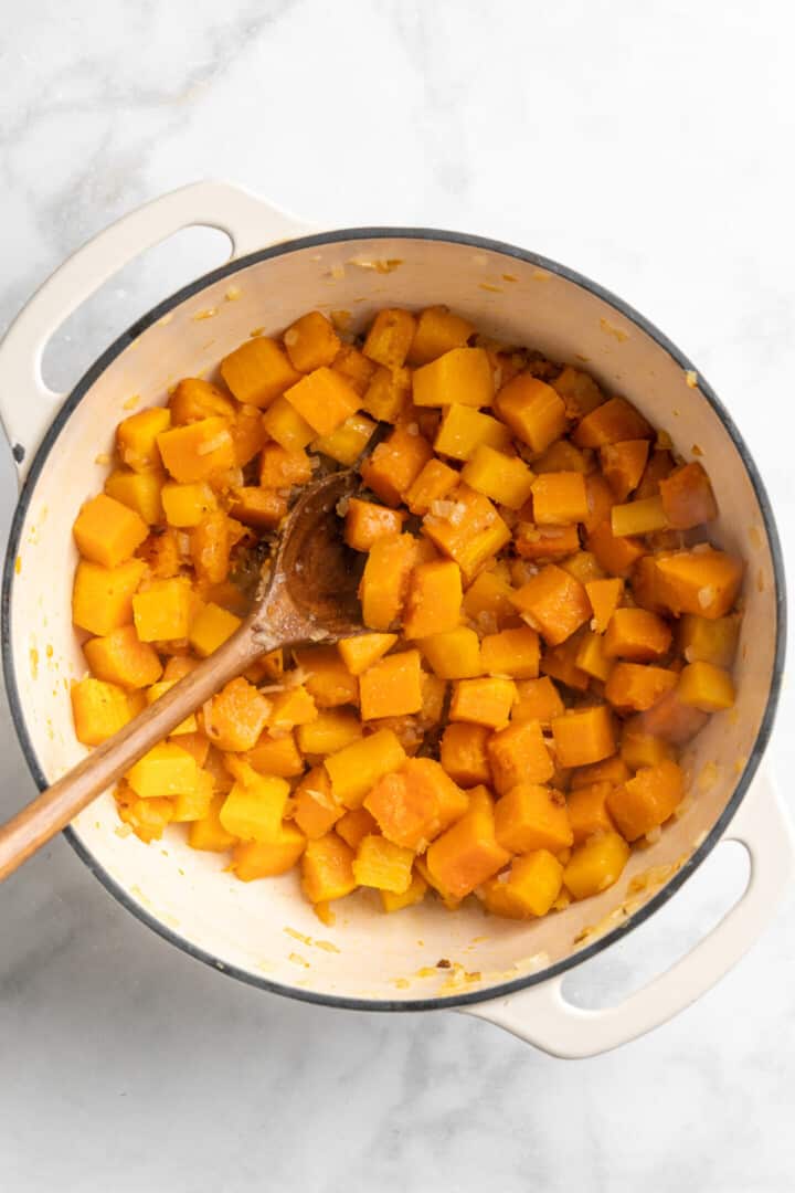 Overhead view of cubed butternut squash in large pot with wooden spoon