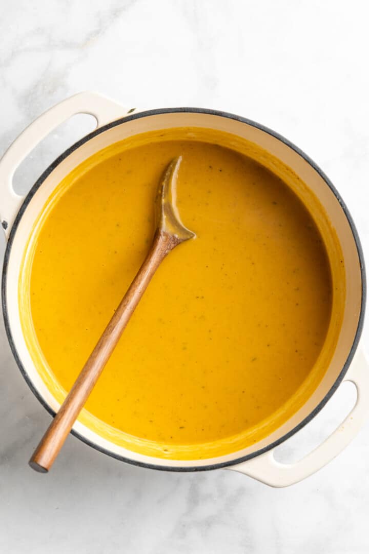 Overhead view of butternut squash soup in pot with wooden spoon