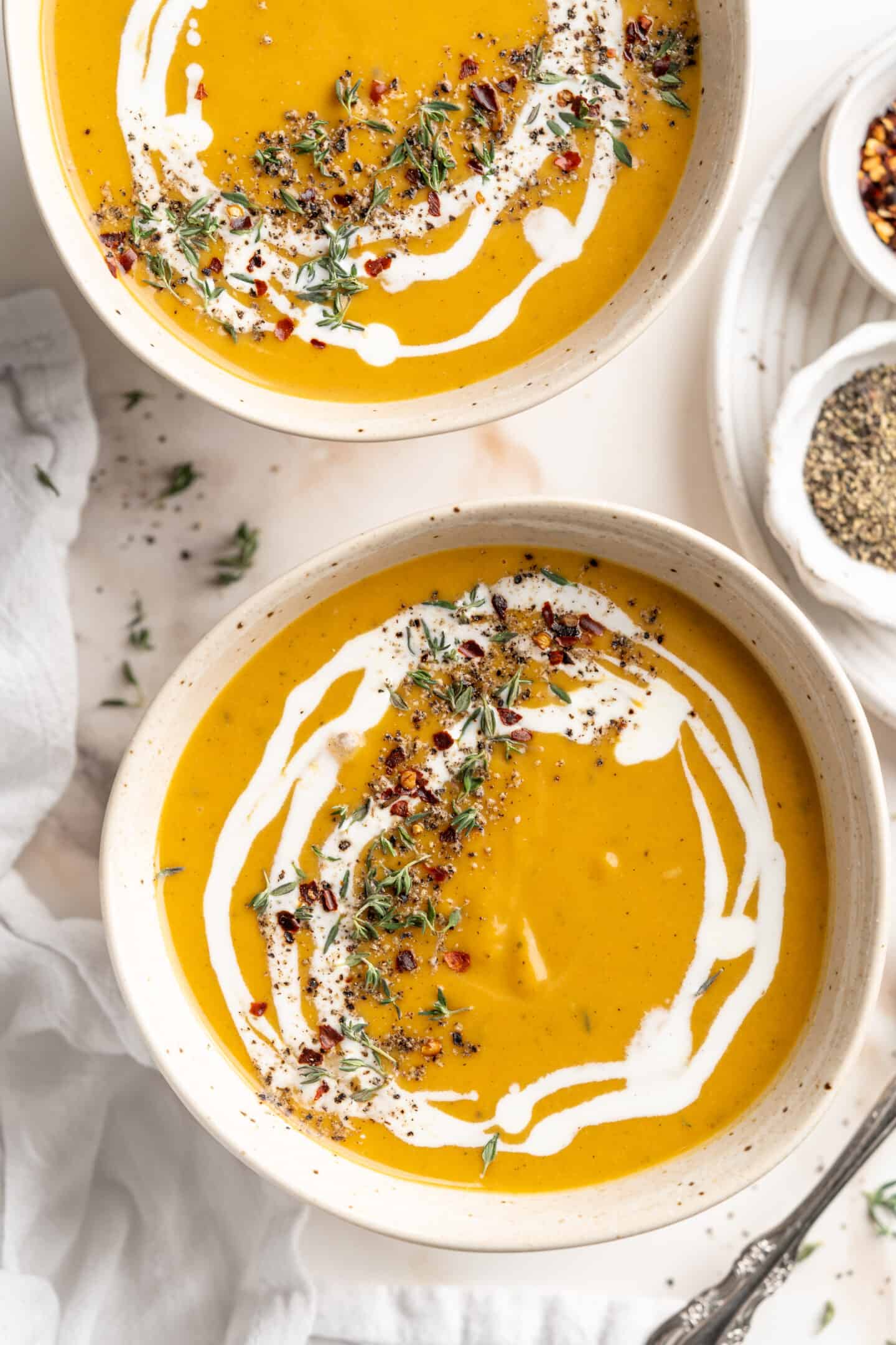 Overhead view of two bowls of butternut squash soup garnished with coconut milk, herbs, and spices