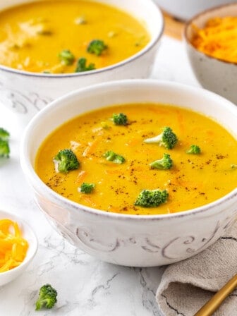 Two bowls of creamy vegan broccoli cheddar soup with broccoli florets for garnish