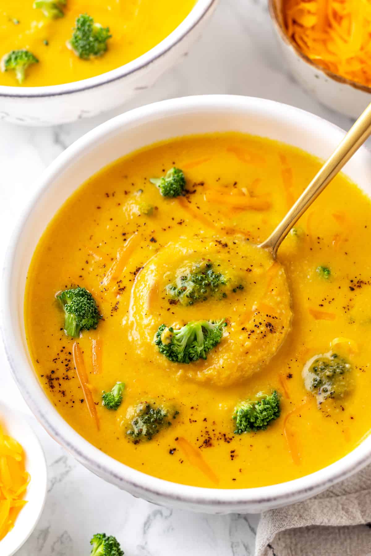 Overhead view of rich, creamy vegan broccoli cheddar soup in bowl with spoon