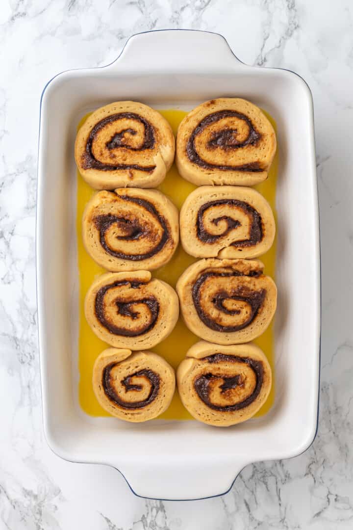 Overhead view of unbaked cinnamon rolls in pan with melted butter