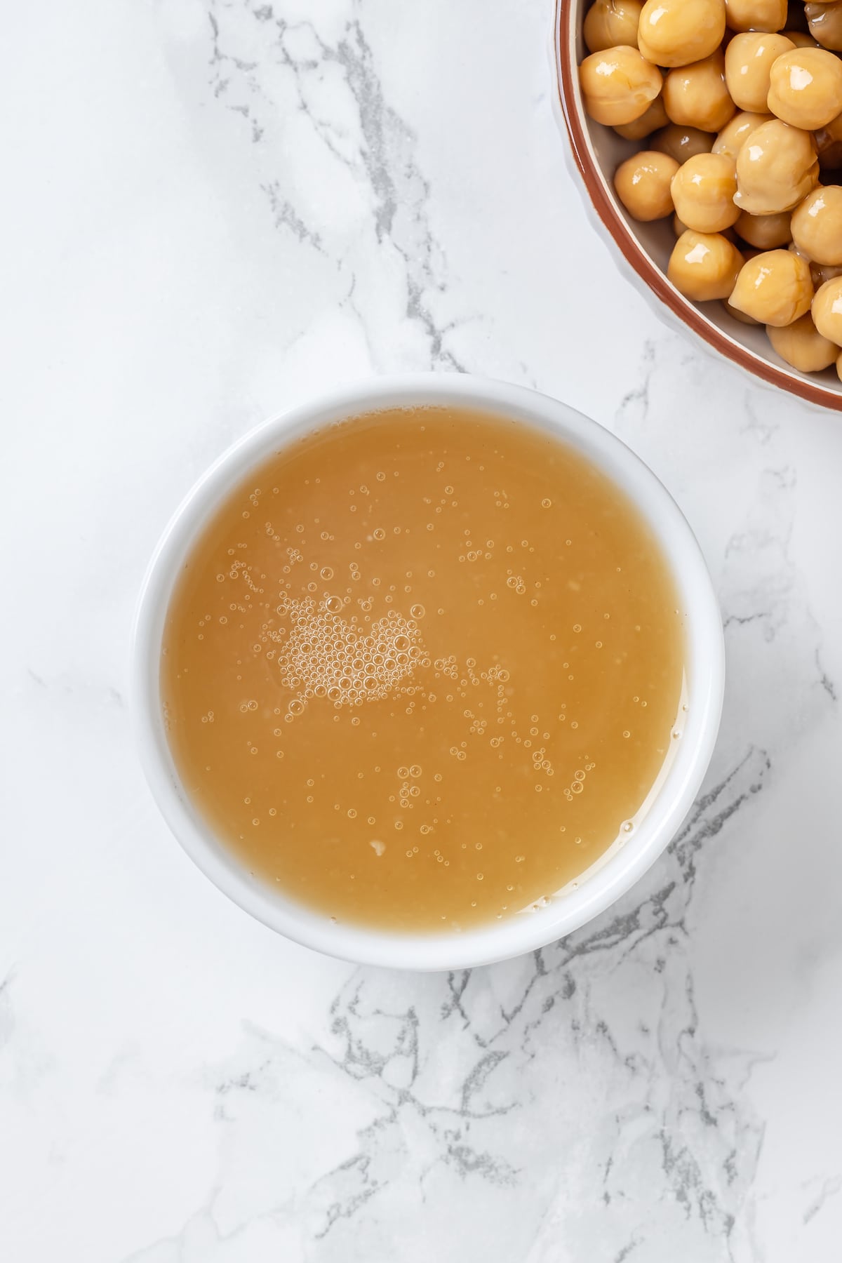 Overhead view of chickpea liquid in small white bowl