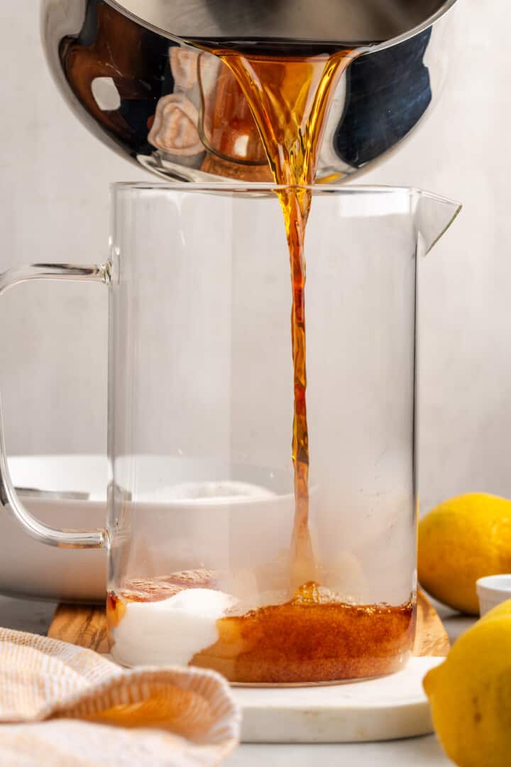 Pouring tea mixture into pitcher with sugar and baking soda