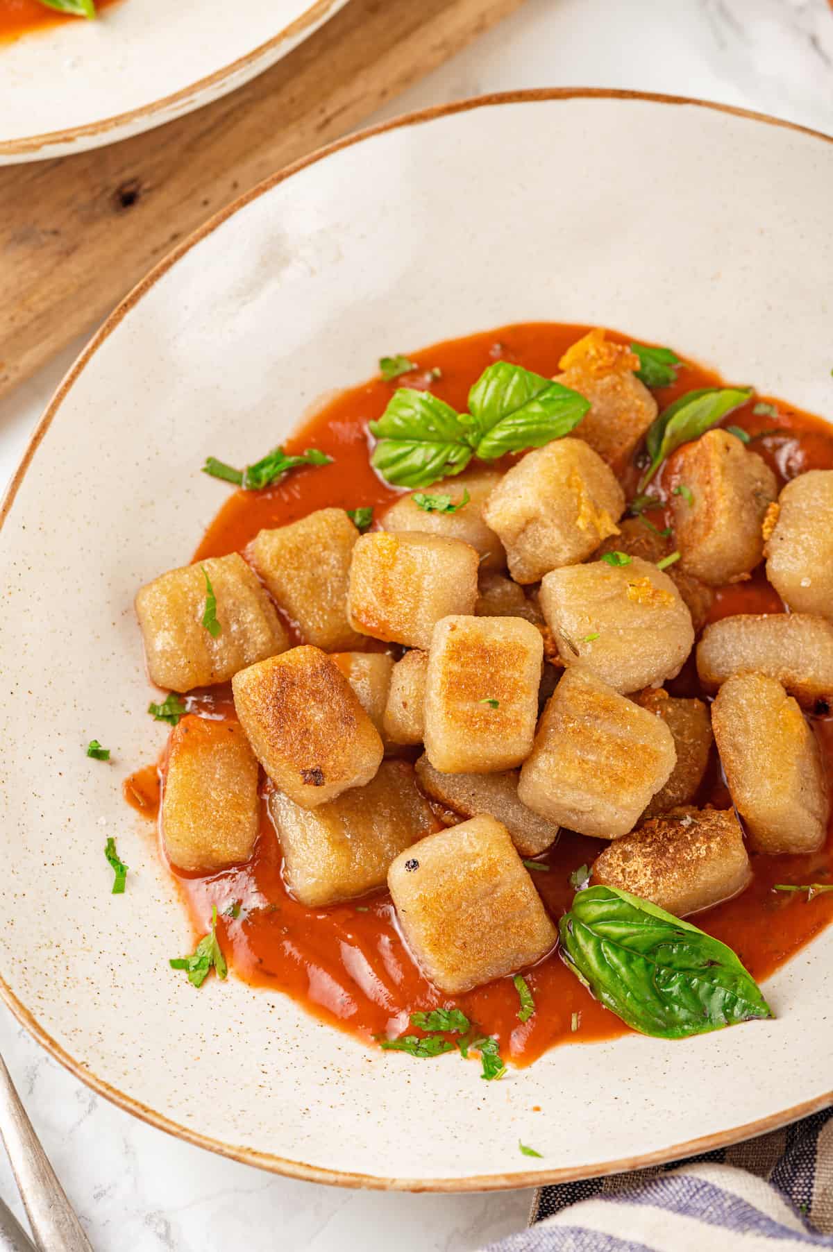 This homemade cauliflower gnocchi is crisp and pillowy, perfect for pairing with your favourite sauces. Easy to make with 5 ingredients! Plate of golden cauliflower gnocchi with marinara and fresh basil leaves.