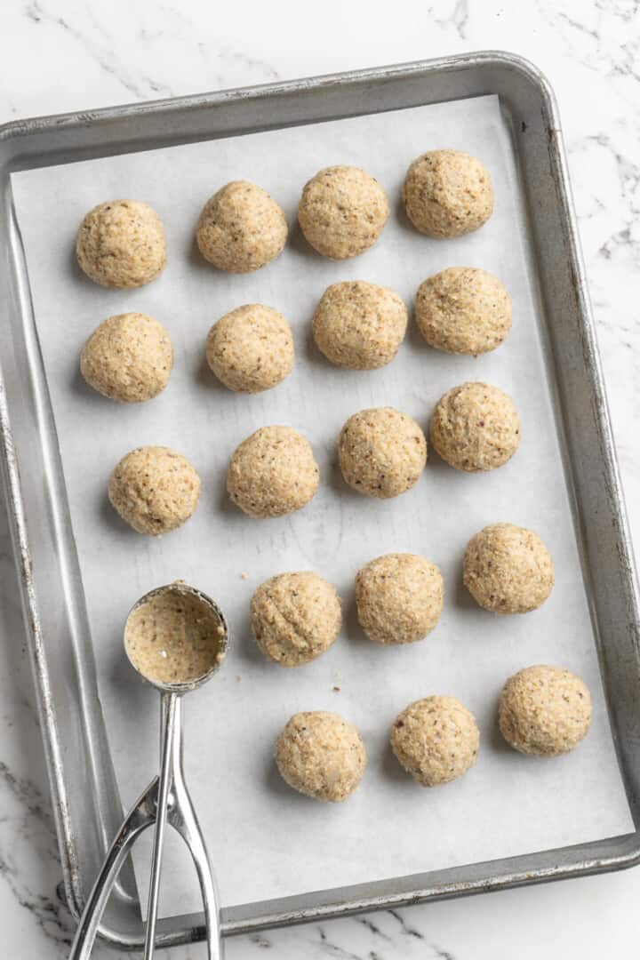 Overhead view of cookie dough scoop set on sheet pan of rolled meatballs