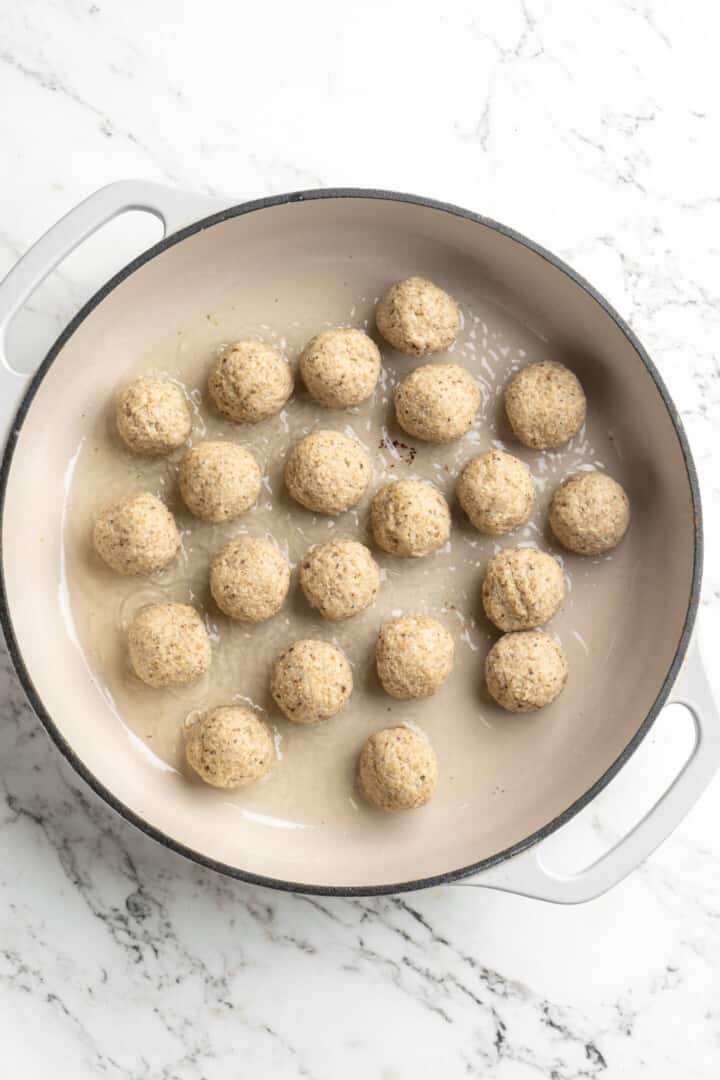 Overhead view of uncooked vegan meatballs added to pan of oil