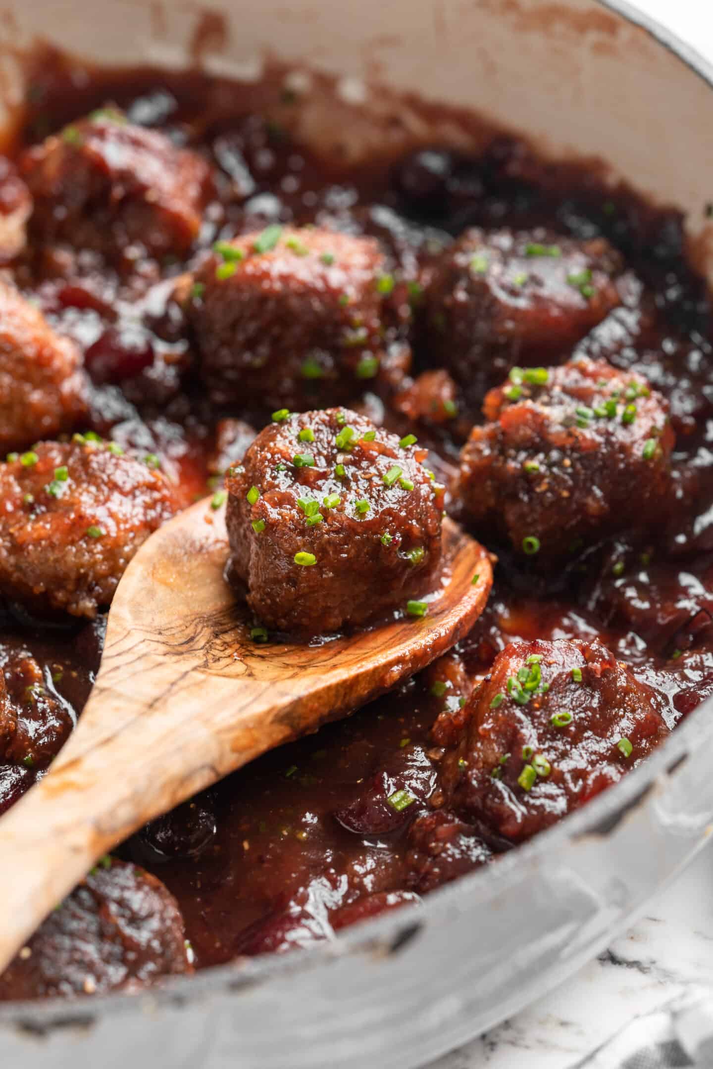 Skillet of vegan cranberry meatballs with wooden spoon lifting meatball from pan