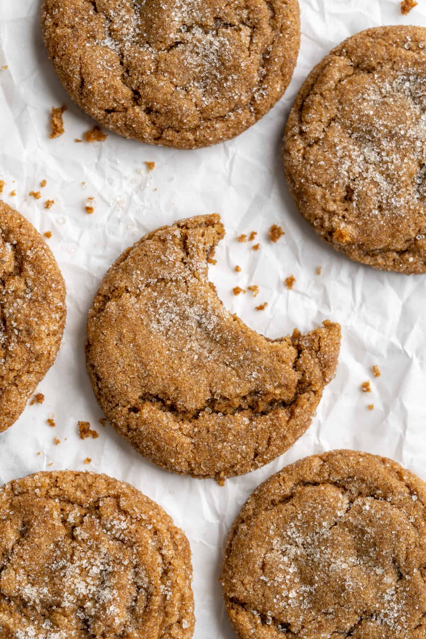 Overhead view of gingersnap molasses cookies on parchment, with middle cookie bitten