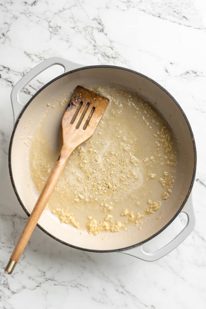 Overhead view of butter and garlic in skillet with wooden spoon