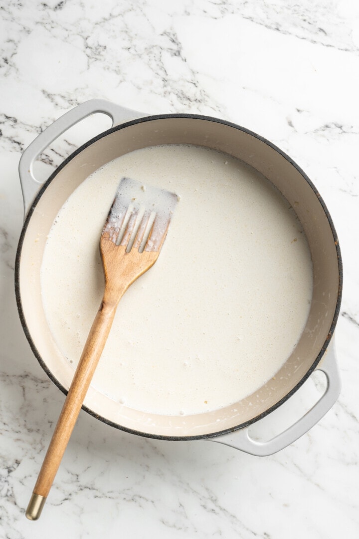 Overhead view of cream poured into skillet with wooden spoon