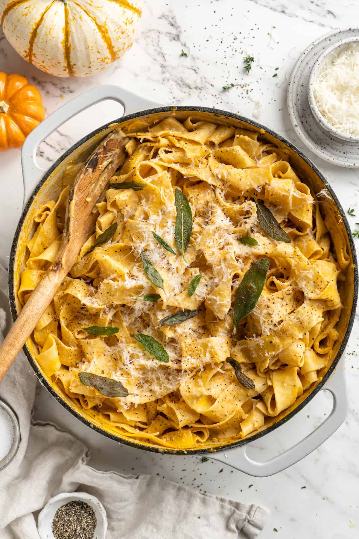 Overhead view of pumpkin alfredo pasta in skillet garnished with sage leaves and parmesan