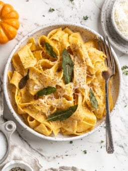 Overhead view of pumpkin alfredo pasta in bowl with fork and crispy sage leaf garnish