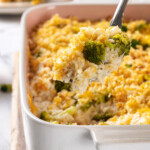 Serving spoon lifting portion of broccoli cheese rice casserole from dish