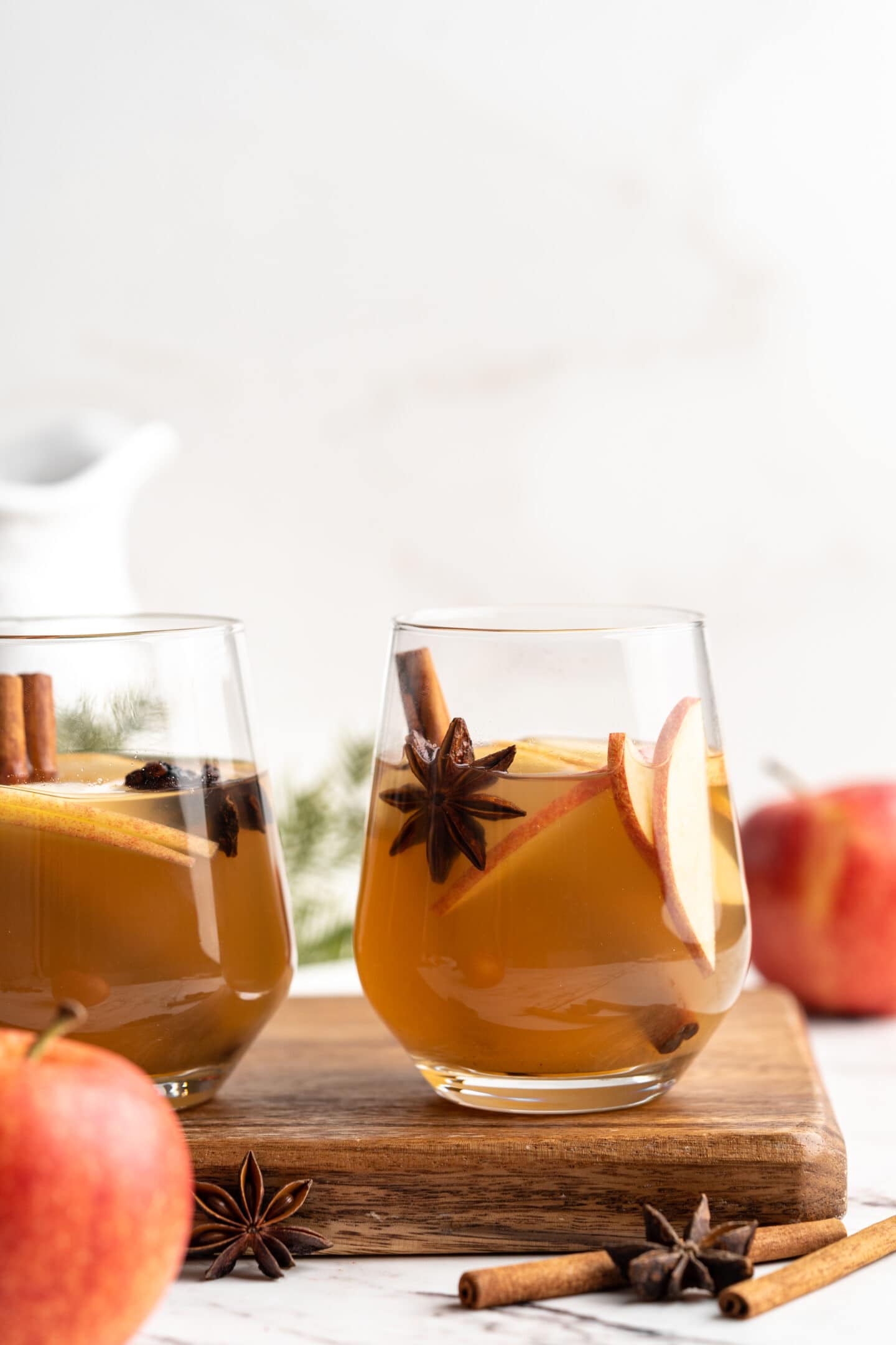 Two glasses of hot spiced apple cider set on wood board