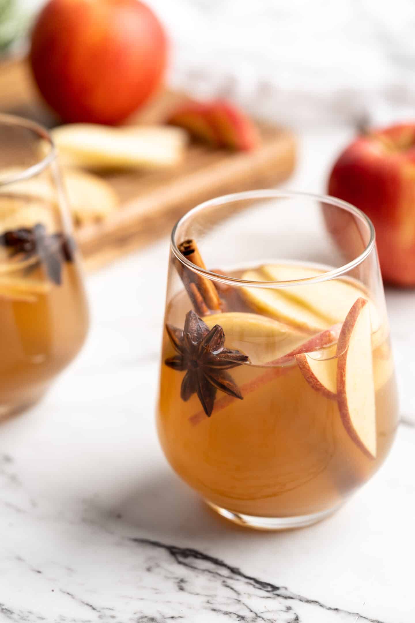 Glass of hot spiced apple cider with apple slices and whole spices for garnish