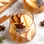 Hot spiced apple cider in glass with whole spices and apple slices