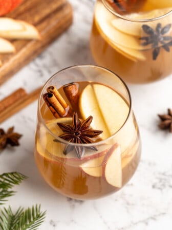 Hot spiced apple cider in glass with whole spices and apple slices