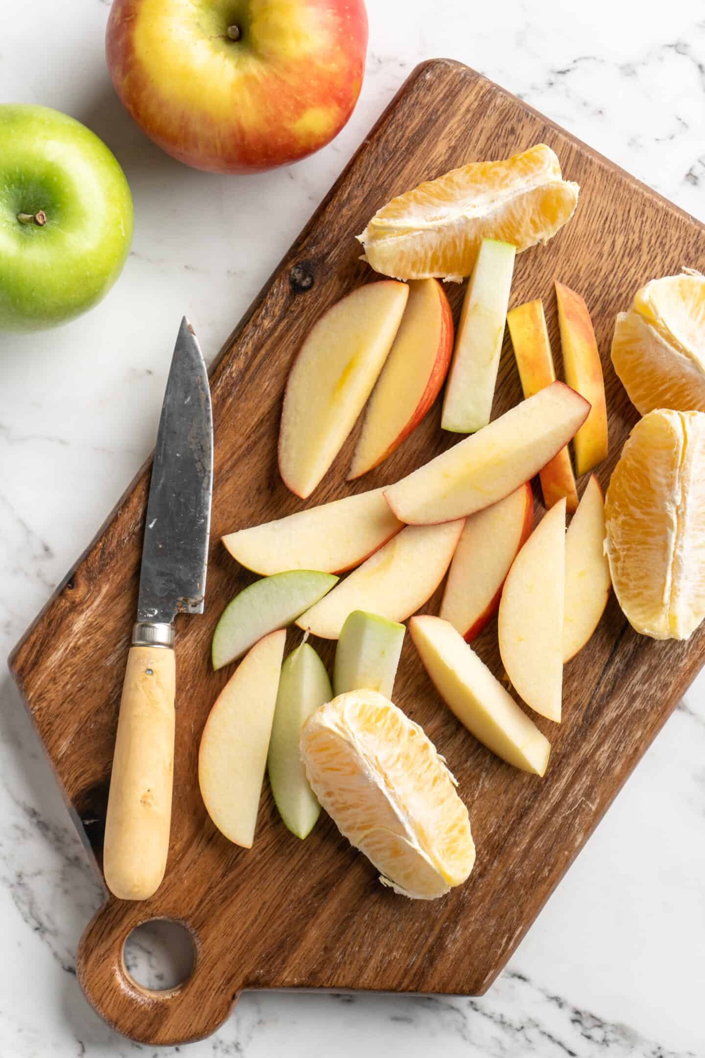 Overhead view of sliced apples and oranges on cutting board with paring knife