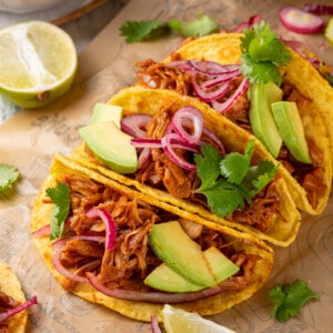 4 jackfruit tacos on parchment paper surrounded by toppings