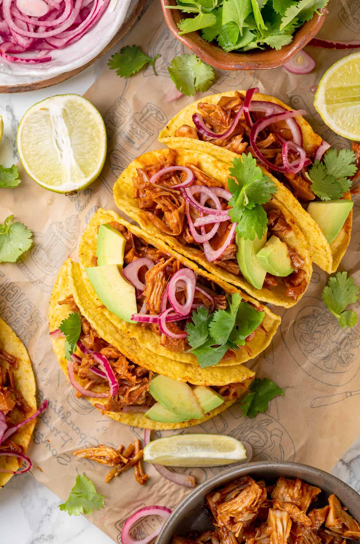 4 jackfruit tacos on printed parchment paper surrounded by toppings