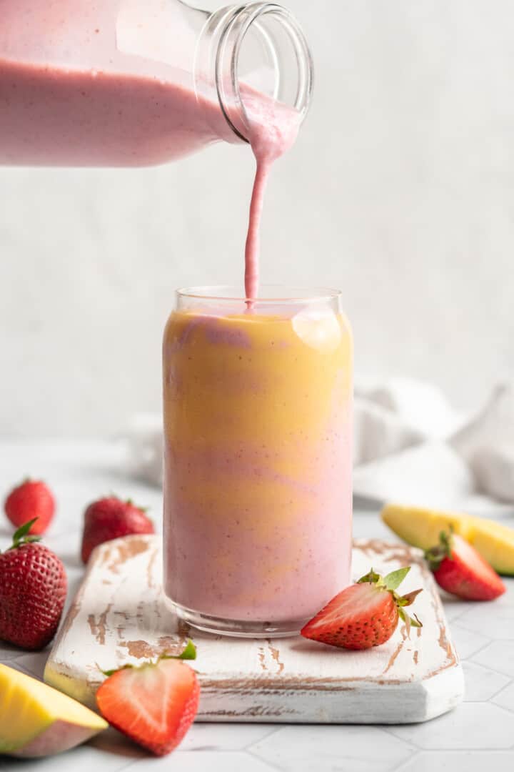 Layered strawberry mango smoothie, with strawberry layer being poured in