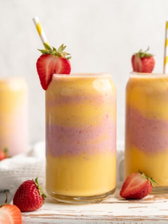 Two glasses of strawberry mango smoothie with straws and strawberries on rim