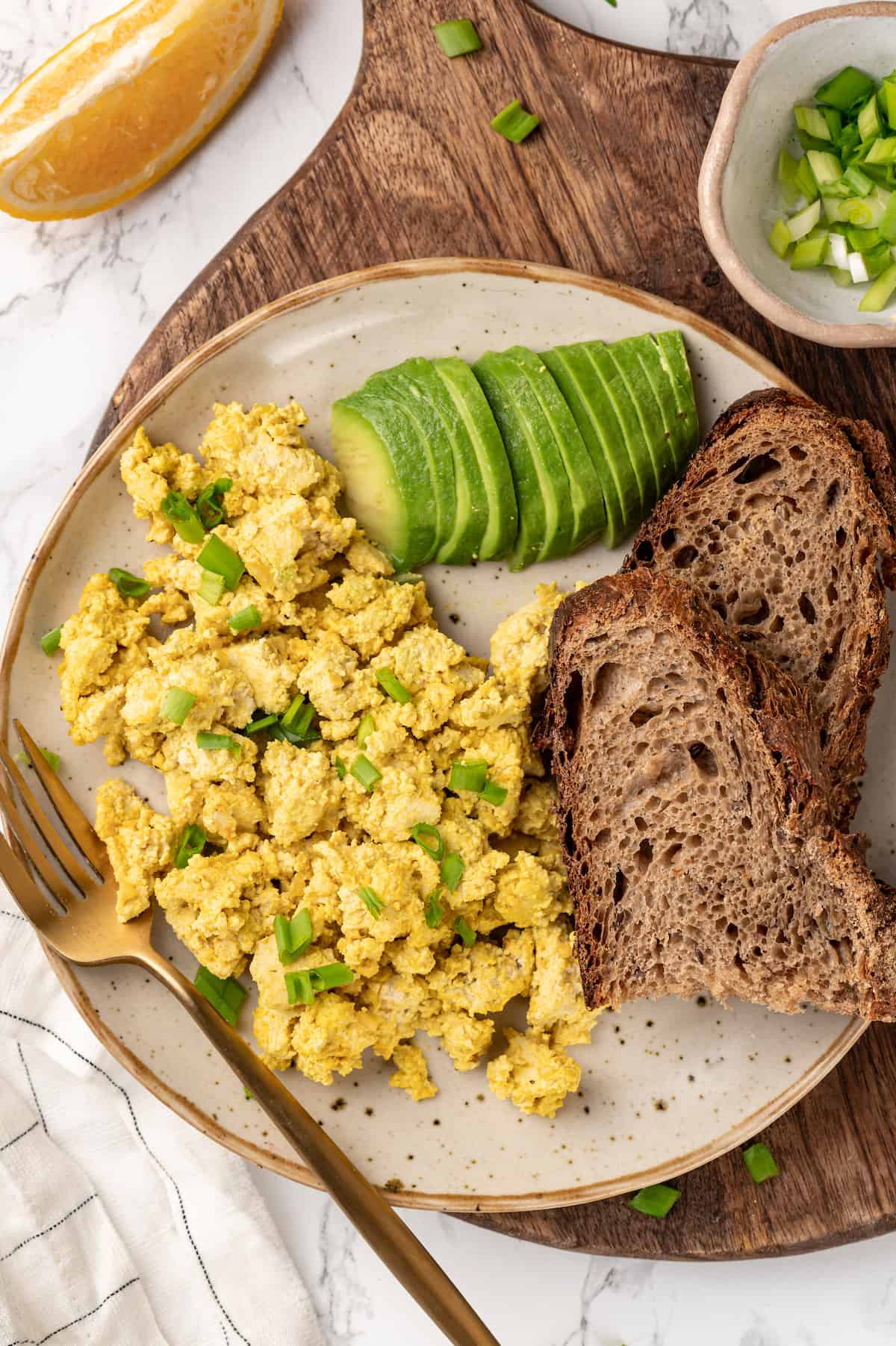 Overhead view of scrambled vegan egg on plate with sliced avocado and toast