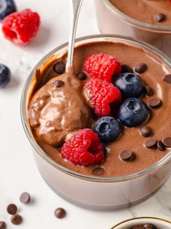 Spoon in bowl of creamy protein pudding topped with berries and chocolate chips