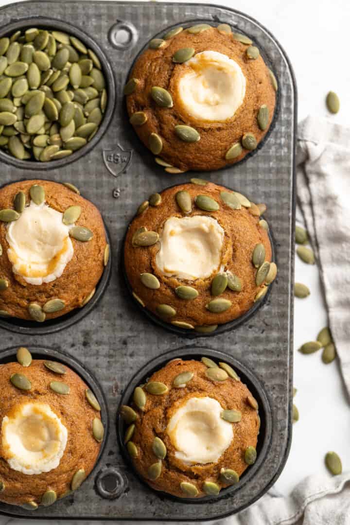 Overhead view of pumpkin cream cheese muffins in pan with pepitas