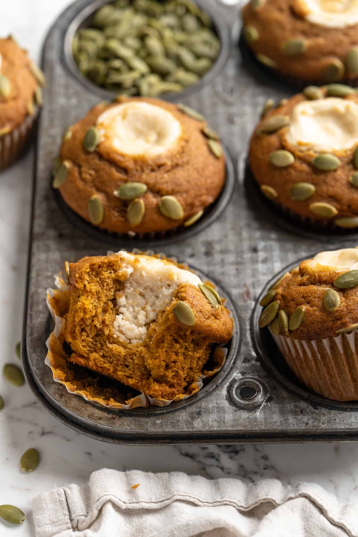 Pumpkin cream cheese muffins in pan, with one bitten into