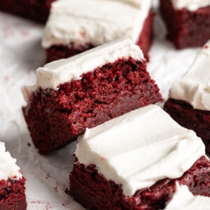Red velvet brownies on parchment paper, with one tipped sideways to show moist crumb