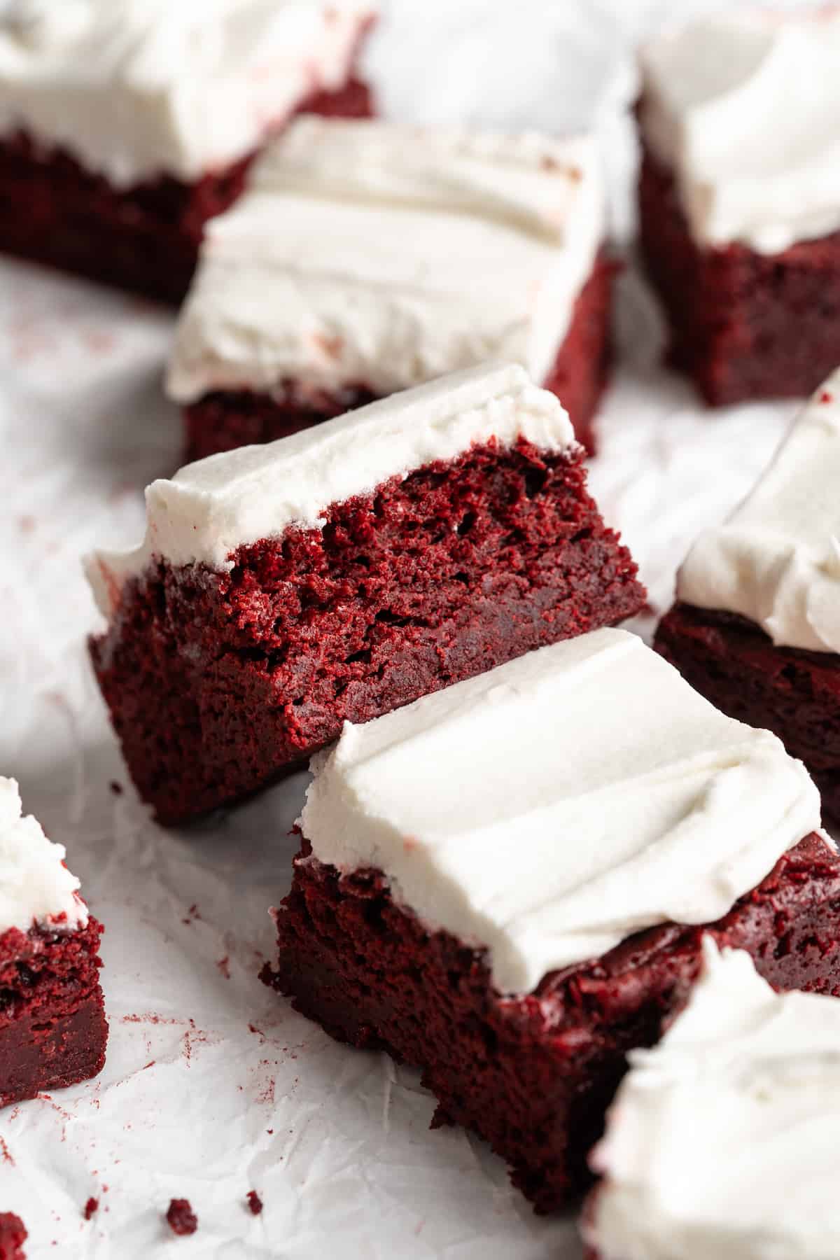 Red velvet brownies on parchment paper, with one tipped sideways to show moist crumb